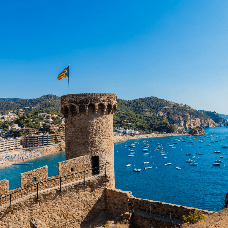 Een kasteel in Tossa de Mar met op de achtergrond de zee met veel bootjes